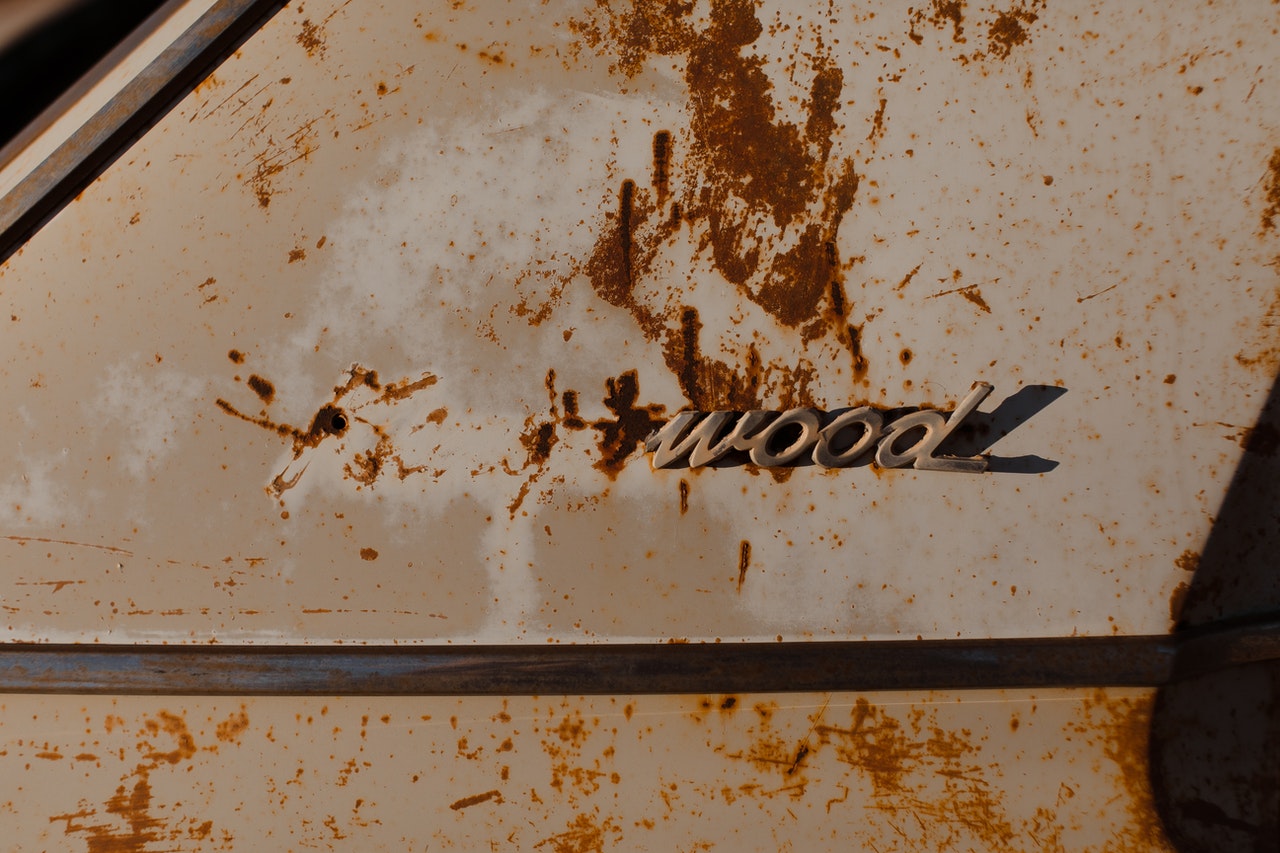 A rusted car with half its badge missing - the word 'wood' is still legible