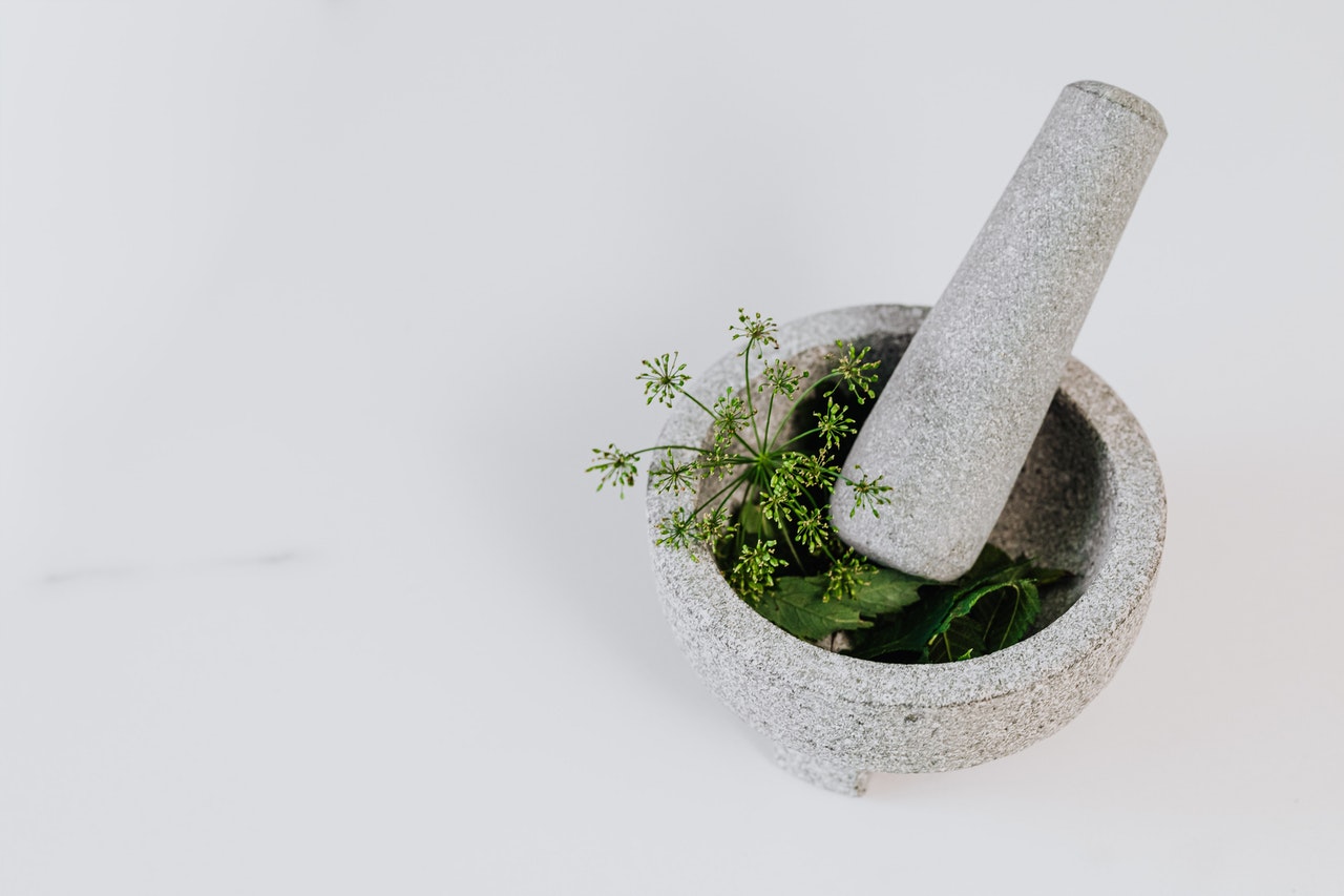 a light grey mortar and pestle with green herbs sticking out of the top