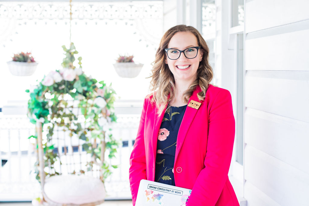 Melissa, a fair-skinned woman and wavy hair, with quirky glasses, a bright pink blazer and a navy dress, smiling and looking to camera.